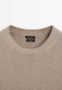 Pull beige à col rond côtelé avec étiquette de marque visible cousue à l'intérieur du col sur un fond blanc.