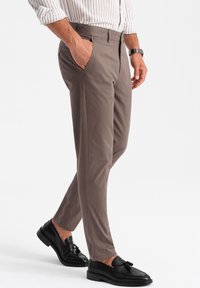 Khaki tapered broek van gladde stof, met zijzakken en een vlakke voorkant. Zwarte loafers met franje-detail maken de look af.