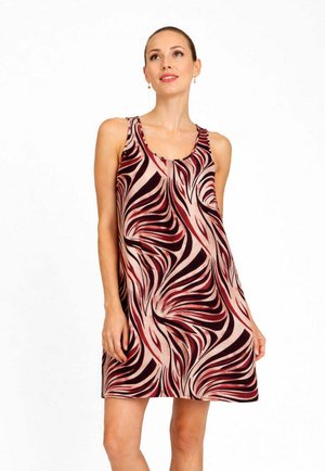 Donna che indossa un vestito senza maniche, lungo fino al ginocchio, con un motivo astratto e vorticoso rosso, rosa e nero, in piedi davanti a uno sfondo bianco semplice.