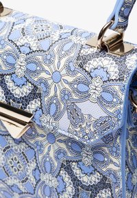 Sac à main bleu à motifs avec des dessins floraux complexes, surface texturée et accents métalliques dorés, équipé d'une sangle bleu clair.