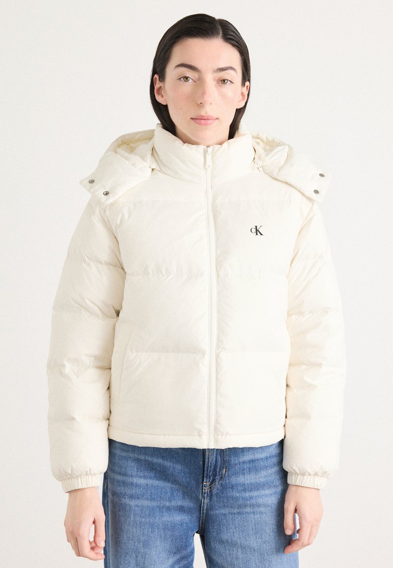 Puffjakke i off-white farge med høy krage, frontglidelås, elastiske mansjetter og logo på brystet. Glatt, polstret tekstur.