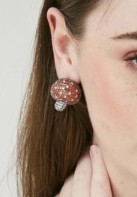 Orange och klara kristallstudsörhängen formade som svampar, med en texturerad, rundad design och en mindre accent.