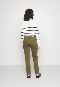 Sweater listrado em branco e marinho com mangas longas, combinado com calças verdes oliva com bolsos laterais e um rótulo castanho na parte de trás.