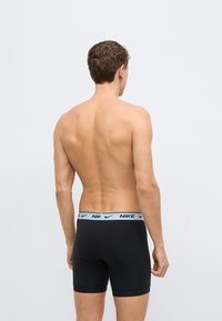 Fekete boxeralsó világoskék elasztikus derékpánttal, amelyen a "NIKE" márkajelzés látható. Simább textúrájú, testhezálló, mintázat nélküli.