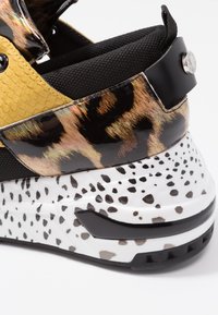 Sort og gul sneaker med tekstureret slange-mønster, glinsende leopard-tryk accenter og en hvid spraglet sål.