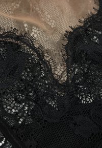 Zwarte kantstof met bloemenpatronen die overlappen op een neutrale netachtergrond, met intricate randen en variërende textielstructuren.