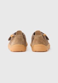 Une paire de chaussures décontractées en daim marron et tissu avec des semelles en caoutchouc beige, vues de l'arrière sur un fond gris clair uni.