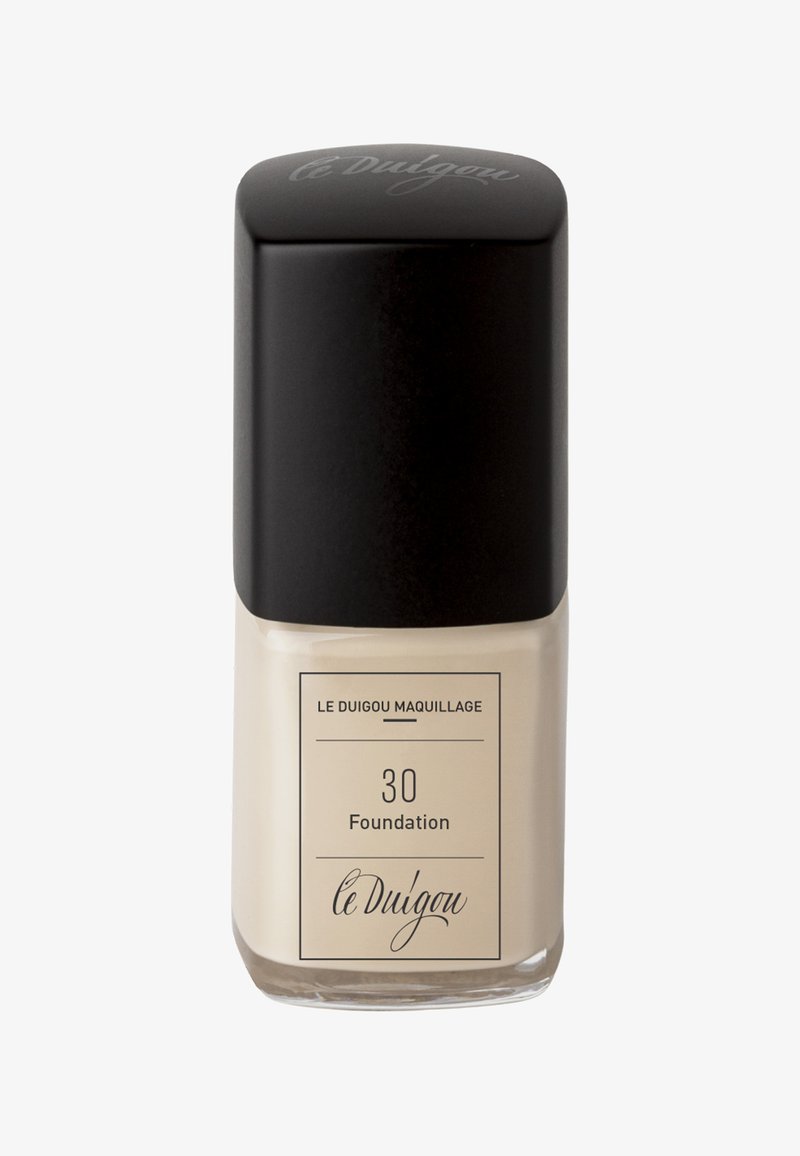 Foundation-Produkt in einer Glasflasche mit beiger Farbe, einem schwarzen quadratischen Deckel und einem Etikett mit den Aufschriften "le Duigou", "30" und "Foundation."