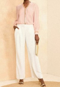 Blusa rosa con rifiniture in paillettes, pantaloni bianchi a gamba larga e tacchi con dettagli dorati; borsa dorata in mano; tessuto liscio e design elegante.