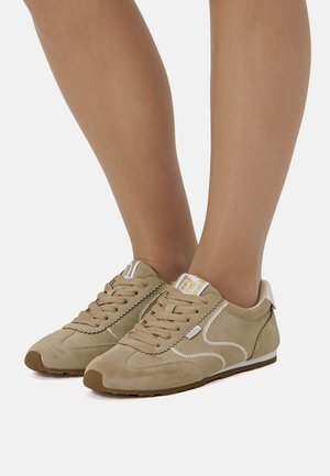 Beige suède sneakers met veters, witte stiksels en een lichtgekleurde hielstrop. Rubberen zool met een afgeronde neus en een eenvoudig ontwerp.