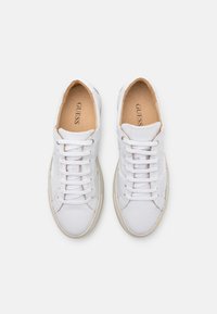 Baskets en cuir blanc avec lacets, bout rond et intérieur beige. Logo "GUESS" gaufré sur le côté et sur la languette. Semelle en caoutchouc.