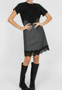 Top nero con dettagli in pizzo abbinato a un vestito a quadri grigio con orlo in pizzo nero, indossato con stivali neri fino al ginocchio.