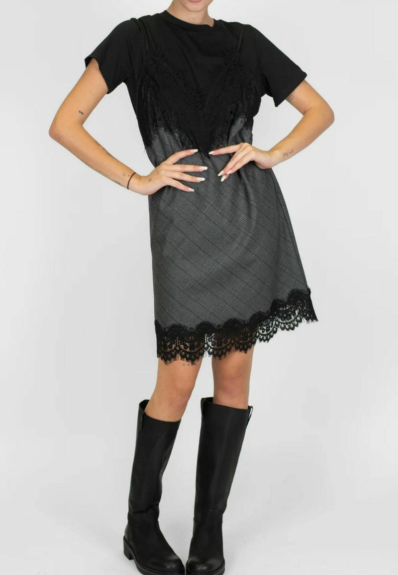 Top nero con dettagli in pizzo abbinato a un vestito a quadri grigio con orlo in pizzo nero, indossato con stivali neri fino al ginocchio.