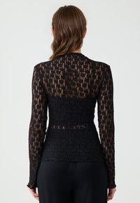Top nero a maniche lunghe con un motivo a trama trasparente e vita aderente. Il tessuto presenta un delicato design simile a pizzo, con cuciture discrete.