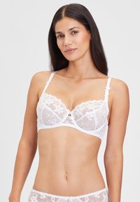 Weißer Spitzen-BH mit floraler Stickerei und durchsichtigen Einsätzen, verstellbaren Trägern und einer dekorativen zentralen Schleife. Glatte Textur.