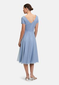 Robe bleu clair avec un corsage ajusté, des manches courtes et un dos en V. Jupe fluide jusqu'aux genoux, ornée de détails subtils en paillettes.