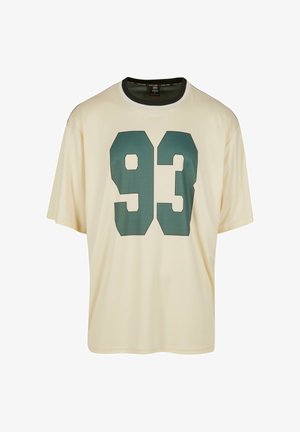 Krema majica s kratkimi rokavi, ki na sprednji strani vsebuje velik zelen "93" grafični motiv. Okrogla ovratnica s kontrastnim obrobo.