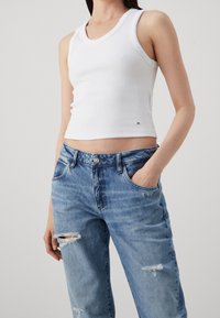 Top in cotone bianco a costine con scollo rotondo, abbinato a jeans chiari strappati con vestibilità rilassata e tasca laterale.