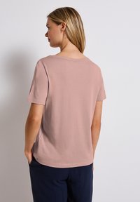 Světle růžové tričko s krátkým rukávem a kulatým výstřihem, s hladkou měkkou strukturou, v kombinaci s tmavými kalhotami, z pohledu zezadu.