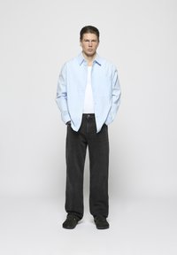 Lichtblauwe lange mouwen shirt, wit T-shirt eronder, zwarte wijde broek en donkere schoenen, met een rechte snit en minimale details.