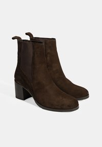 Bruine suède enkellaarsjes met een blokhak, voorzien van elastische zijkanten en treklabels voor gemakkelijke aan- en uittrekken, een gladde textuur en een ronde neus.