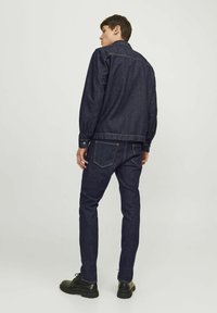 Chaqueta de mezclilla y jeans en azul oscuro, con un diseño clásico, cierres de botón y una textura suave, llevados con botas negras.
