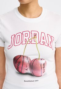 T-shirt blanc avec le texte rouge "JORDAN", un graphisme de deux cerises conçues comme des ballons de basketball avec des tiges vertes, et "Établi en 1984" en dessous.