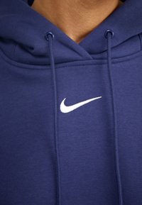 Sweatshirt azul marinho com uma textura suave, apresentando um logo branco da Nike no peito e dois cordões no pescoço.