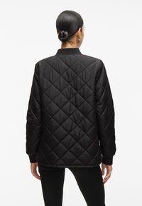Černá prošívaná bunda s diamantovým vzorem, žebrovanými manžetami a kulatým výstřihem. Materiál působí hladce s matným povrchem.