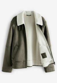 Chaqueta de piel sintética marrón con forro de felpa blanca, que presenta un cuello de borreguito, cierre de cremallera y dos bolsillos laterales.