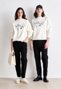 Sweatshirts blancs avec des impressions éclaboussées colorées, pantalons noirs, un sac fourre-tout beige, baskets blanches et bottes noires. Design simple et décontracté.