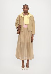 Beige cropped takki kevyen vaaleanpunaisen paidan päällä, yhdistettynä nopeasti viuhtautuvaan vaaleabeigeen untuvahameeseen ja valkoisiin kärkipohjaisiin korkokenkiin. Ruskea käsilaukku kultaisilla yksityiskohdilla.