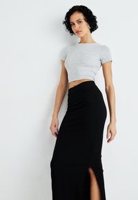 Grå kortermet t-skjorte kombinert med et svart ribbet maxiskjørt med sideslit, begge i en tettsittende design og glatt tekstur.