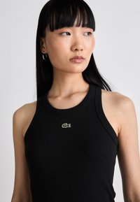 Schwarzes geripptes Tanktop mit rundem Ausschnitt, das auf der Brust ein kleines grünes gesticktes Krokodil-Logo zeigt. Slim-Fit-Schnitt.