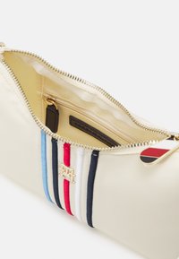 Rechthoekige crèmekleurige tas met een gouden rits, voorzien van meerkleurige strepen (blauw, rood, wit en marineblauw) en een gouden logoakkoord.