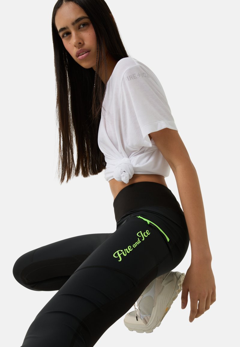 Schwarze Sportleggings mit grütem "Fire and Ice"-Text, Reißverschlusstasche und glatter Oberfläche, kombiniert mit einem weißen geknoteten T-Shirt.