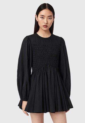 Musta mekko, jossa on röyhelöity vartalo, pitkät hihat ja levenevä helma. Valmistettu kevyestä kankaasta, jossa on sileä pinta.