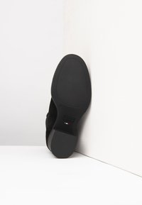Scarpa in suede nera con una suola liscia e arrotondata. La parte inferiore presenta un design minimalista e un piccolo accento con la bandiera italiana.