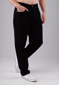 Schwarze Jeanshose mit geradem Bein, verfügt über fünf Taschen und Details aus Kupfer. Kombiniert mit weißen Turnschuhen.