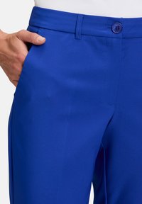 Jasně modré kalhoty s hladkým povrchem, s knoflíkovým zapínáním a bočními kapsami. Pas je přiléhavý, což zajišťuje štíhlý vzhled.