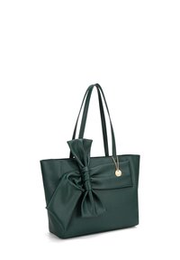 Borsa a tracolla verde con una grande decorazione a fiocco sul davanti, due manici lunghi e un ciondolo d'accento dorato attaccato.