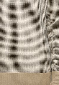 Sweater de malha em padrões castanho e creme com um design texturizado em xadrez; apresenta uma bainha sólida bege na parte inferior.