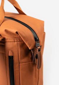 Borsa in pelle arancione con zip nera, dotata di accenti cuciti e una tasca laterale. Primo piano del dettaglio superiore e della zip.