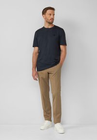 Marineblaues T-Shirt mit kurzen Ärmeln und einem schlichten Design, kombiniert mit khakifarbenen Hosen und weißen Sneakers. Verfügt über ein kleines Logo auf der Brust.