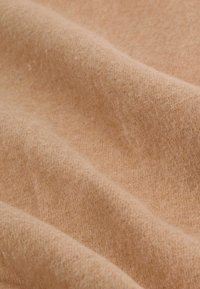 Miękki beżowy materiał wełniany o delikatnej strukturze dzianiny oraz subtelnych fałdach tworzących łagodne cienie na powierzchni.