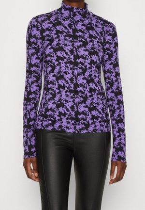 Zwart en paars bloemenpatroon, langärmelig coltrui-top, gedragen met zwarte leren broek, zichtbaar van schouders tot heupen.