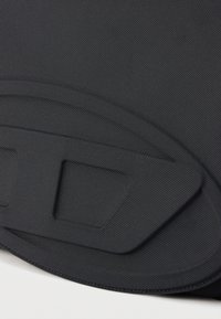 Προϊόν από μαύρο υφασμάτινο ύφασμα με υφή, με καμπυλωτό σχέδιο και στρωματοποιημένες λεπτομέρειες. Διαθέτει ένα μικρό ορθογώνιο στοιχείο στο κέντρο.