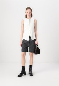 Hvite ermeløse vester med knapplukking, kombinert med mørke denimshorts, svarte ankelstøvler og en liten brun håndveske. Enkel design.