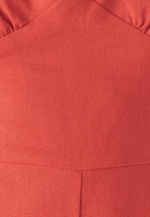 Close-up van koraalkleurige stof met zichtbare weefstructuur en naaddetails op een kledingstuk met geraffineerde bovenranden.