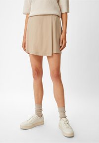 Beige indpakning mini nederdel med en glat tekstur og subtil plissering. Kombineret med lysfarvede sneakers og ribbede sokker.